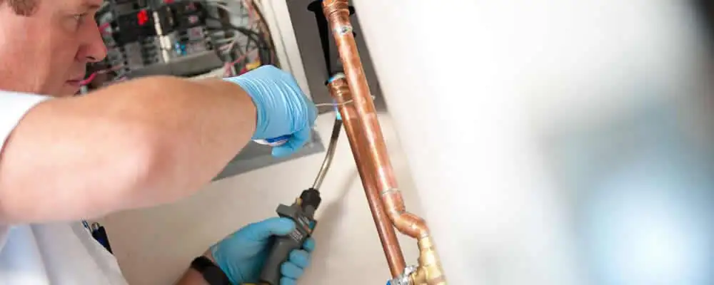 Water heater repair technician testing copper pipe connections and controls in Scottsdale, AZ